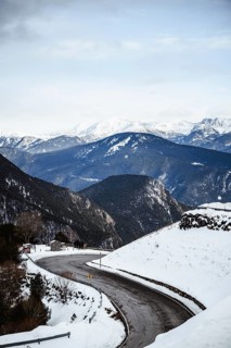 A winding road cuts through a snow covered valley amidst towering mountain peaks under a serene