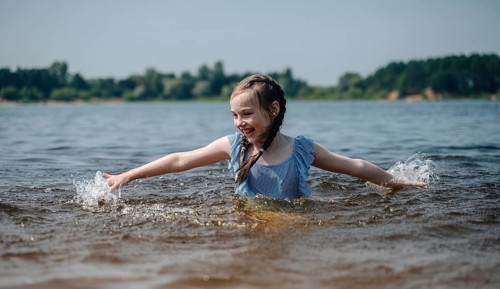 A cheerful young girl splashes playfully in the water, enjoying a sunny day outdoors. Her happiness