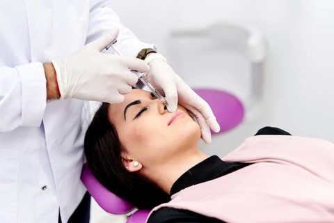 A medical professional administers a cosmetic facial injection to a woman lying on a treatment