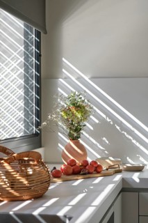 A modern kitchen boasts a peaceful ambiance with sunlight streaming through the blinds,