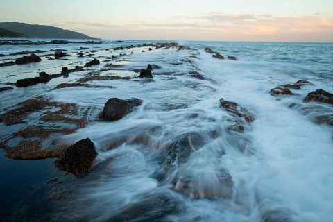 Coastal view of Tarifa, Cadiz, captured at sunset with gentle waves flowing over rocky terrain.