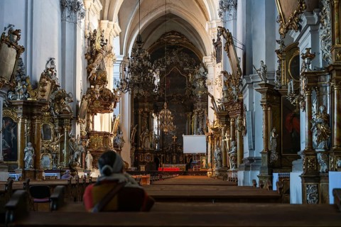 Grand interior of a baroque church featuring ornate golden altars and chandeliers with a person
