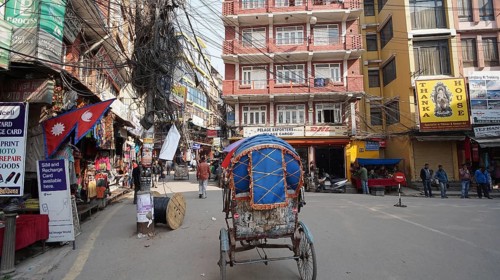 A street scene with a rickshaw, colorful buildings and a jumble of power lines on a pole in the