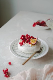 Beautifully arranged red currant and passionfruit pavlova on a white ceramic plate placed on a
