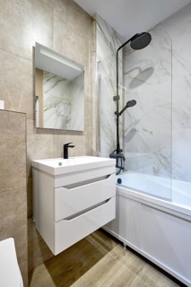 This modern bathroom features a sleek bathtub, a rainfall showerhead on a marble wall, and a