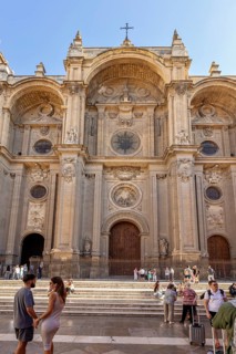 Magnificent baroque cathedral façade with people in front of it under a blue sky, Granada
