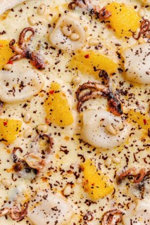 Close up view of a gourmet pizza topped with octopus, squid, slices of orange, mozzarella cheese,