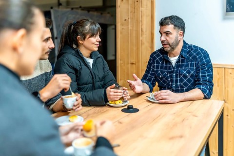 Friends sitting around a wooden table in a cafe, enjoying coffee and tea while having a lively