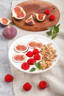 Yoghurt with raspberry, granola and figs in white plate on a gray concrete background and linen