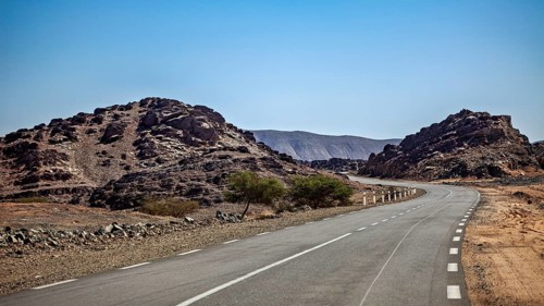 Lonely road between rocky desert hills under a clear blue sky, roads through the Sahara in Algeria