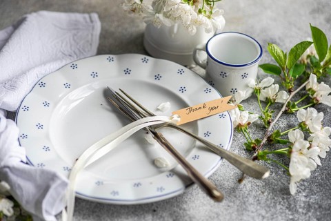 A beautifully set table with a white plate, cutlery, and a thank you note, adorned with delicate