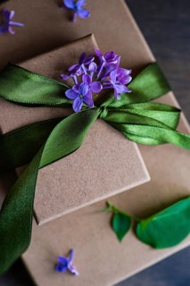 A beautifully wrapped gift box adorned with a vibrant green ribbon and delicate purple flowers. The