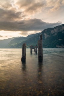 Old wooden pier posts rise from the still waters of Walensee in Switzerland, framed by dramatic