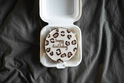 Top view of a bento birthday cake with happy birthday lettering in a white takeout box, set against