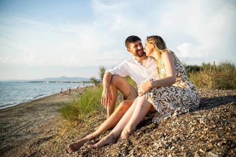 A couple sits affectionately on an Italian beach, enjoying a sunny day. The tranquil sea and clear