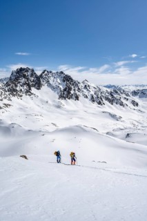 Two ski tourers in mountain landscape with snow, view of summit Piz Vadret, ascent to Scalettahorn,