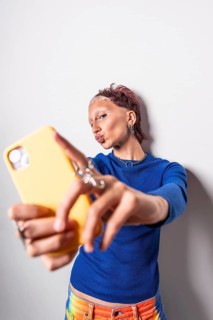Fashionable woman in vibrant, colorful trousers takes a selfie with a yellow smartphone. She wears