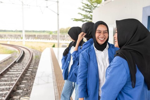 A group of Asian Muslim women wearing blue uniforms and black hijabs, sharing a laugh while waiting