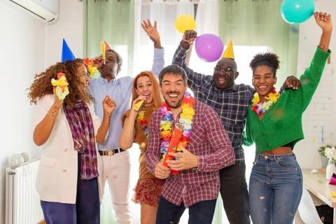 A vibrant group of friends celebrates a birthday indoors. They wear party hats and leis, hold
