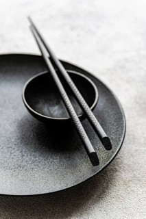 Minimalist black table setting featuring a textured plate, small bowl, and detailed chopsticks. The