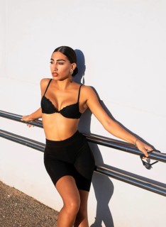 A confident woman leans against a railing, soaking in the bright sunlight. She wears black