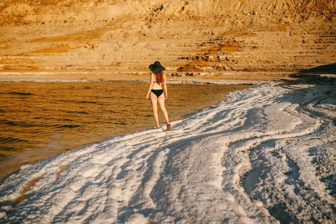 Back view of an unrecognizable woman in a bikini and wide-brimmed hat walking along the salt