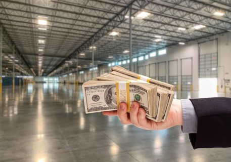 Male Hand Holding Thousands of Dollars Inside Empty Industrial Warehouse