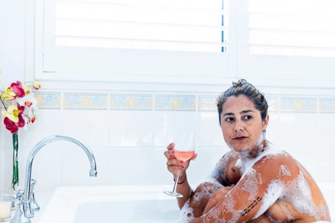 A woman enjoys a serene bubble bath, holding a glass of rose wine. Surrounded by suds and fresh