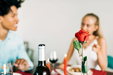 A romantic dinner setting features a red rose, candles, and wine. A couple enjoys an intimate meal,