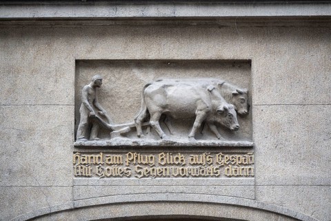 Stone relief depicting a farmer using oxen for ploughing, including a saying in fracture script