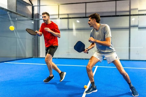 Men actively engaging in a pickleball game on a blue indoor court, holding paddles and reacting to