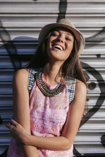 Young woman wearing a straw hat and patterned dress, smiling joyfully in bright sunlight. She