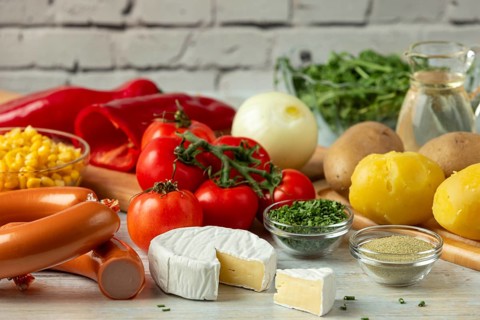 Fresh ingredients such as potatoes, tomatoes, peppers, sausage, corn, onions, cheese and arugula in
