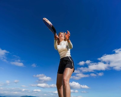 From below a young woman is captured in action while playing tennis outdoors, with a clear blue sky