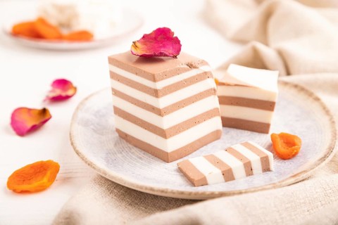 Cocoa and milk jelly with dried apricots on white wooden background and linen textile, side view,