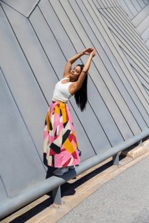 A woman in a vibrant, colorful skirt poses gracefully against a backdrop of striking modern