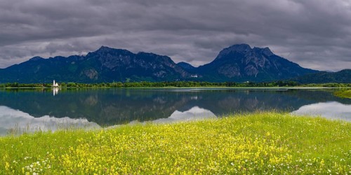 Panorama over a spring meadow and Lake Forggensee, behind it Tegelberg and Säuling, in between