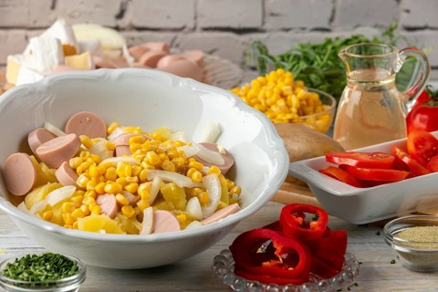 Potatoes, corn, onions and sausage in a bowl surrounded by other ingredients such as peppers,