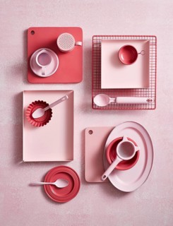 Top view of an array of pink kitchen utensils and crockery on a textured surface, featuring cups,
