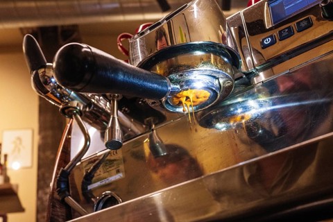 An intricate view of an espresso machine brewing specialty coffee. The rich, golden espresso flows