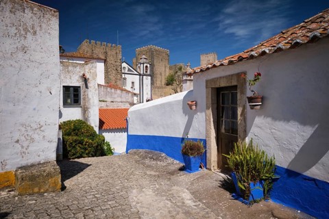 Sunny street scene in Obidos showing whitewashed houses, blue painted walls and the medieval castle