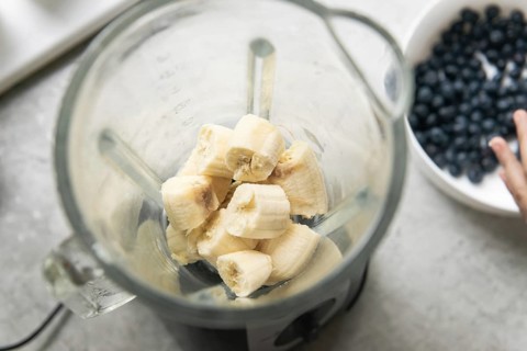 Close-up of chopped bananas in a blender, ready to be blended A bowl of fresh blueberries sits