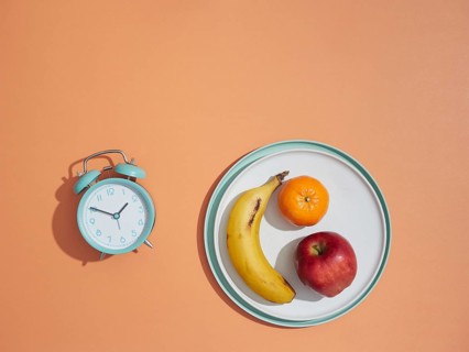 Mealtime, alarm clock and fruits in a plate. Healthy eating concept, dieting, weight loss and