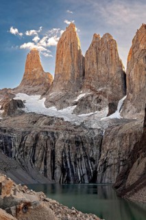 High, sunlit cliffs towering over a calm lake with a clear sky, The rock towers of Torres del Paine