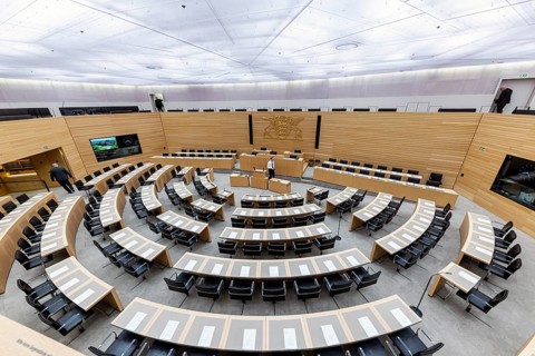 Plenary hall deserted with the seats of deputies and the government bank. Behind it is the coat of