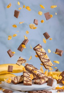 Muesli bars with chocolate and banana float in the air together with cornflakes