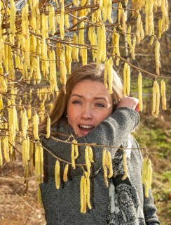 Young Caucasian woman with allergy problem stands by flowering hazel bush and sneezes in the crook