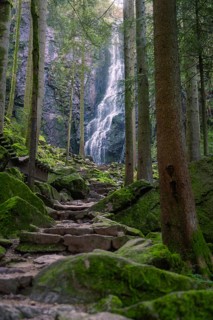 A waterfall in a wooded area with moss-covered rocks and a stony path, Burgbach waterfall, Bad