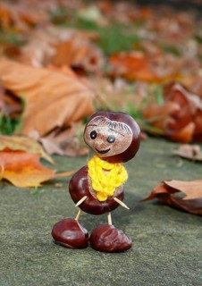 Funny chestnut figure with yellow scarf on a wall in autumn leaves, North Rhine-Westphalia, Germany