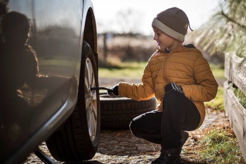 Young boy turns the spanner during changing the wheel in the car